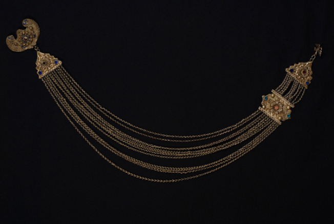 Μπαλτσούδα, αλυσιδωτό κόσμημα μέσης με συρματερές πλάκες, στολισμένες με χρωματιστές γυάλινες πέτρες. Η πλάκα της κορυφής είναι διακοσμημένη με την τεχνική του σμάλτου 