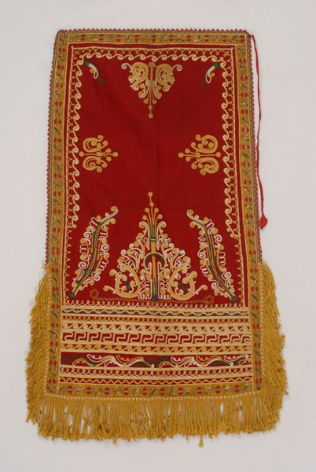 Red felt apron embroidered with colourful outres (cordons) and fringed end