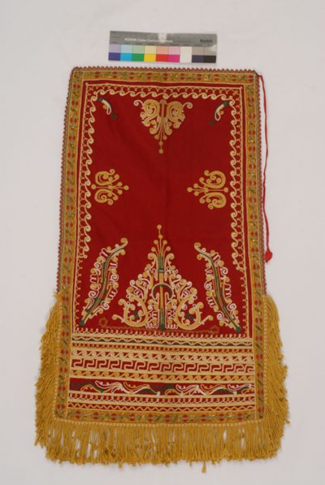 Red felt apron embroidered with colourful outres (cordons) and fringed end