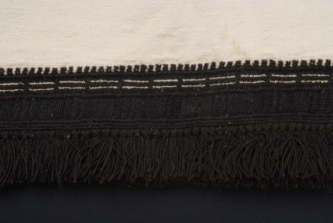 Border, detail of the decoration with thick black embroidery and short woollen tassels
