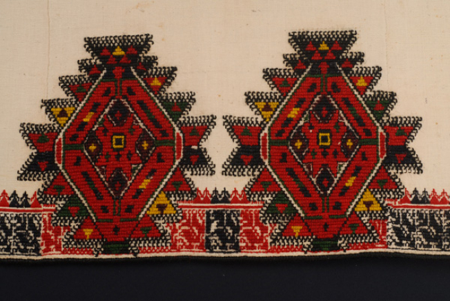 Detail of the embroidered decoration at the border, at the straight back panel: a band with parallelograms and polygonal motifs. Among them, the "dance" of the anthropomorphic motifs.