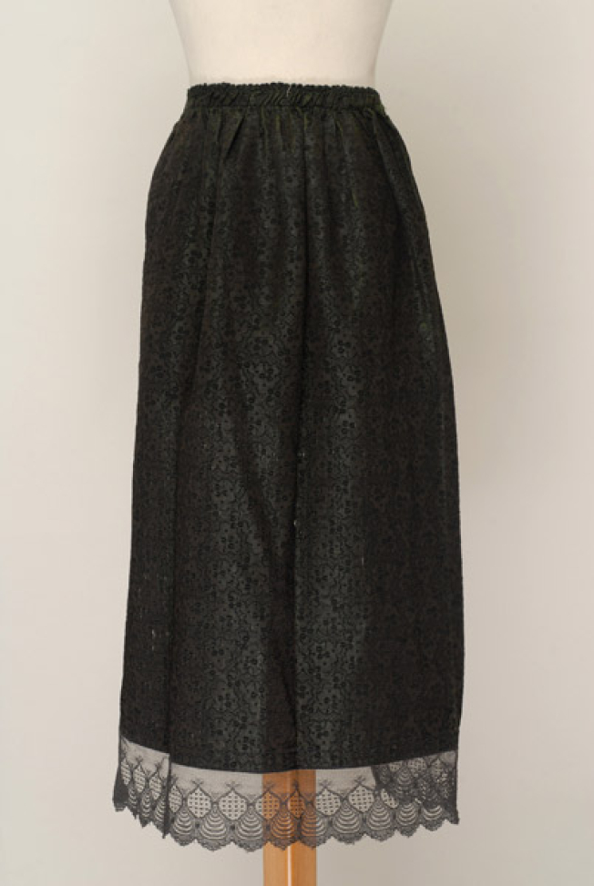 Dark-coloured apron with embellished floral motifs. Edging with lace sold by the metre.