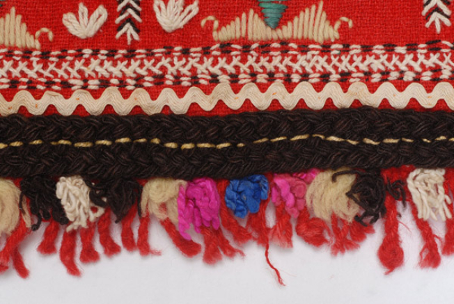 Detail of the decoration, horizontal embroidered band, applique braid, wool gaitani and fringed ends from fullen wool fabric