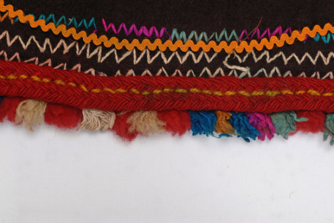 Detail of the decoration, embroidered crooked line, applique wool gaitani (cordon) and polychrome fringes made of fullen wool fabric at the edge
