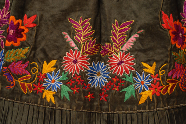 Bottom of the apron, detail of the decoration with multicoloured vegetal motifs, crafted with various stitches (darning stitch, pressed stitch, riza (stem stitch), rococo stitch)