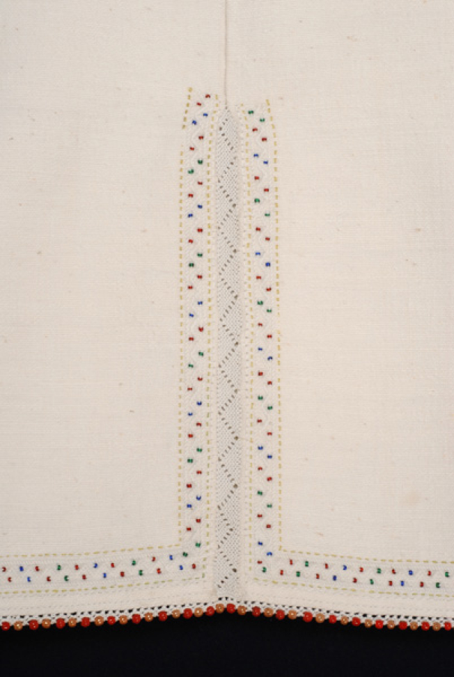 Border, detail of the lacy band of the seam and the embroidered decoration with slip coloured beads 