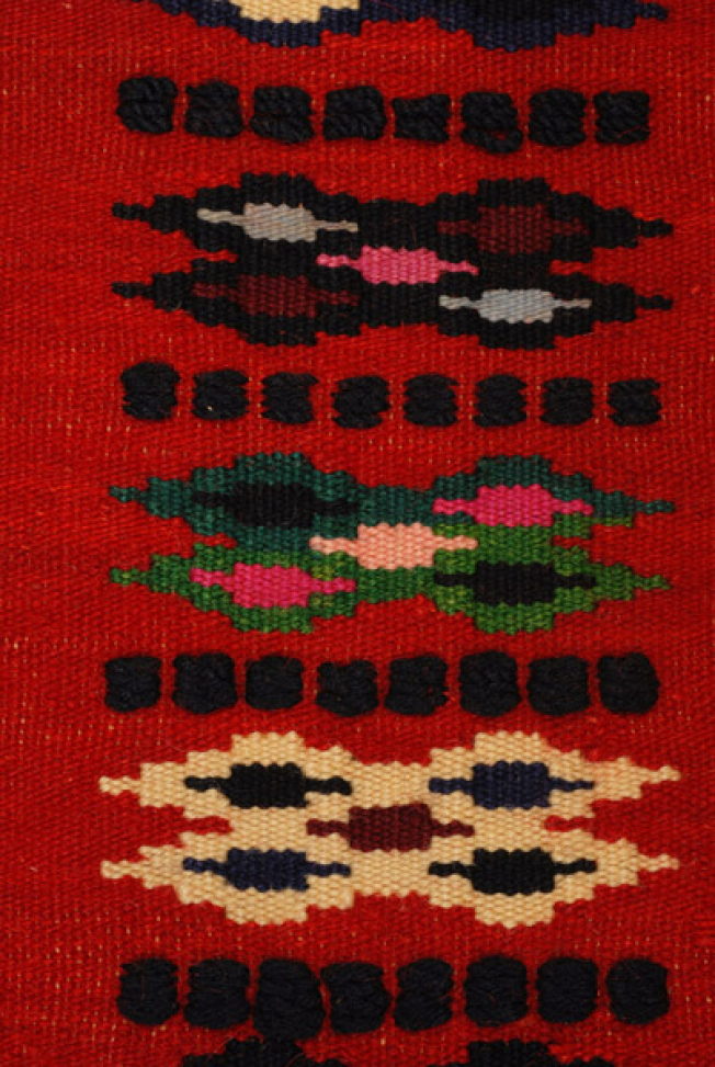 Detail of the embellished decoration: lozenge-shaped motifs separated with black horizontal stripes in the centre of the apron