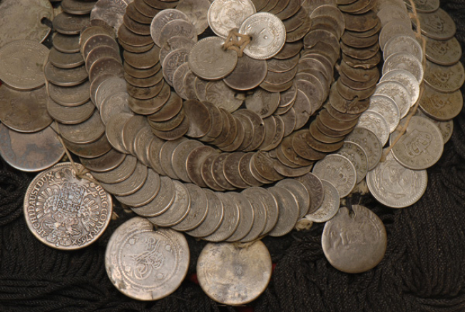 Τα άσπρα, ασημένια νομίσματα, φολιδωτά επίρραπτα σε σπειροειδή διάταξη πάνω στον τιπέ, κόκκινο φέσι.